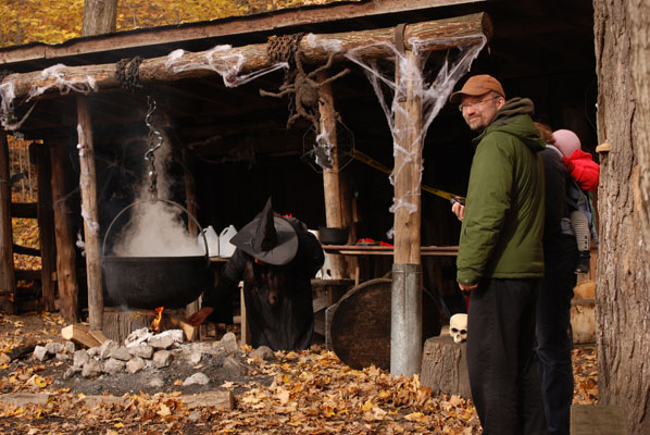 a woman in witch costume checks the fire under her cauldron at a Halloween display at the Kortright Centre for Conservation